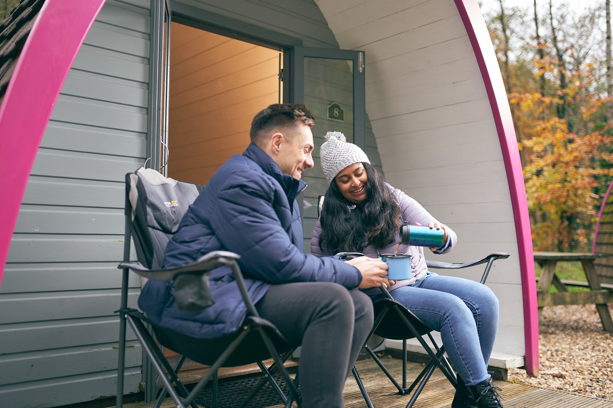 Woman pouring a drink into a mug held by a man both sitting down and smiling
