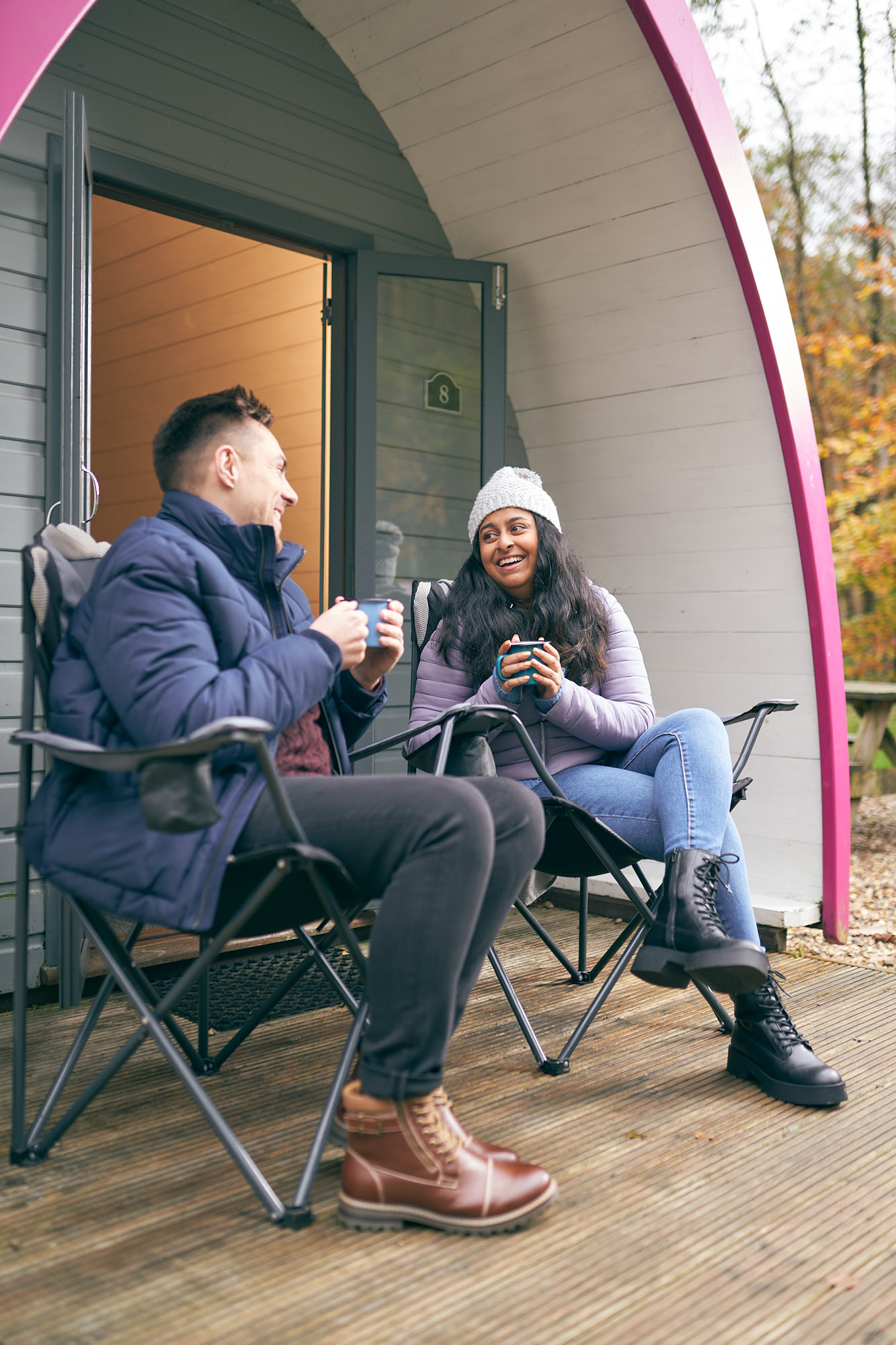 Man and woman sat outside holding mugs laughing