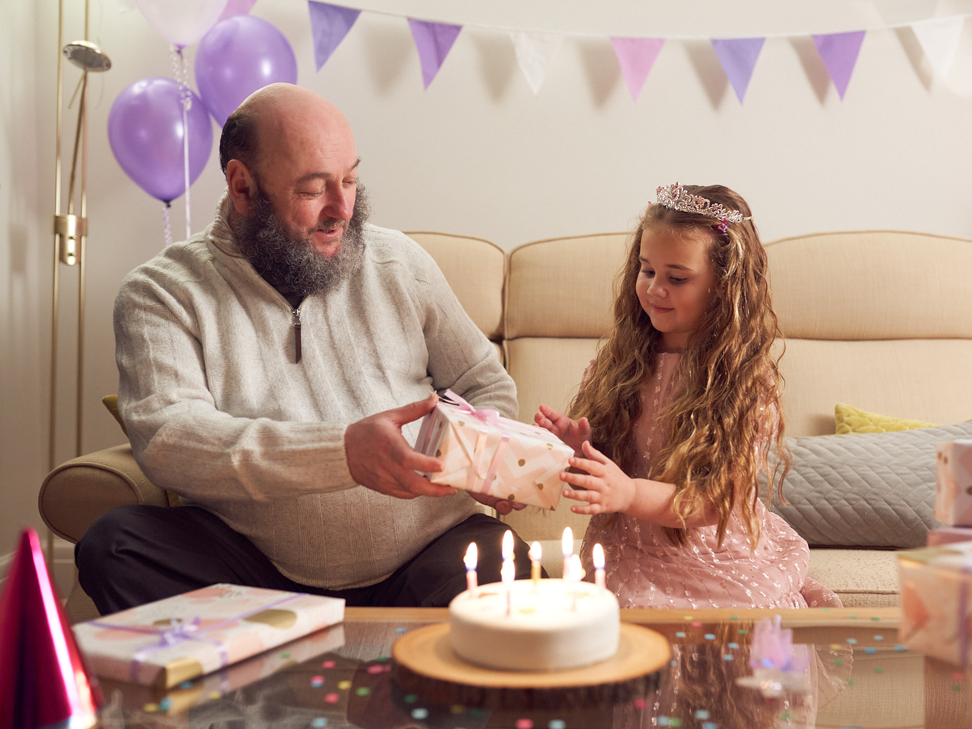 Man passing young girl a present both sat down with birthday decorations around them