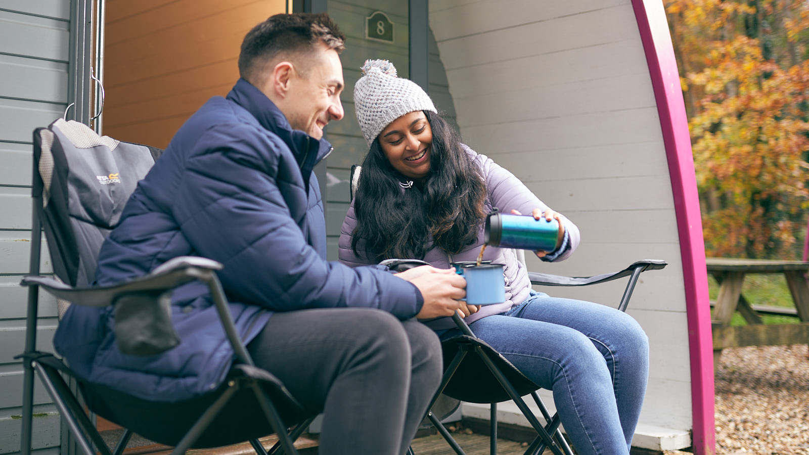 Woman pouring drink into a mug held by a man both sitting down smiling