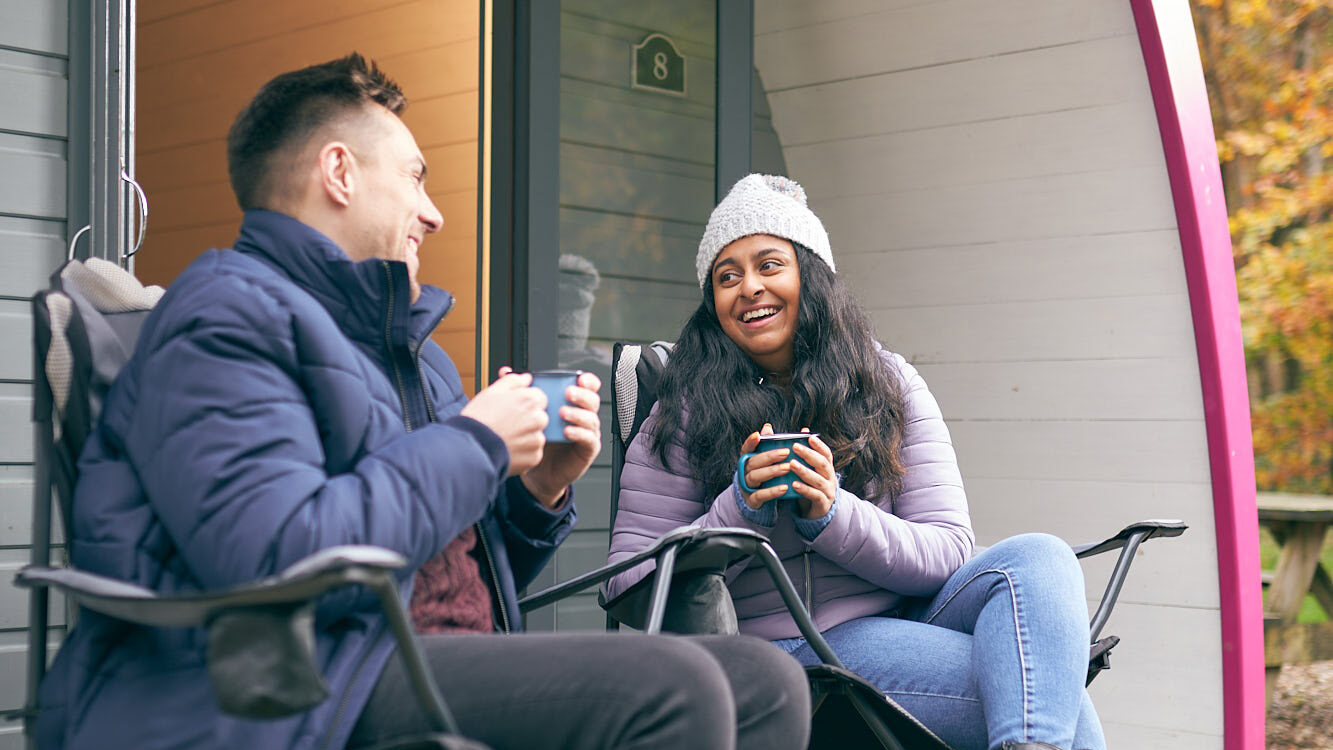 Man and woman sat outside holding mugs laughing