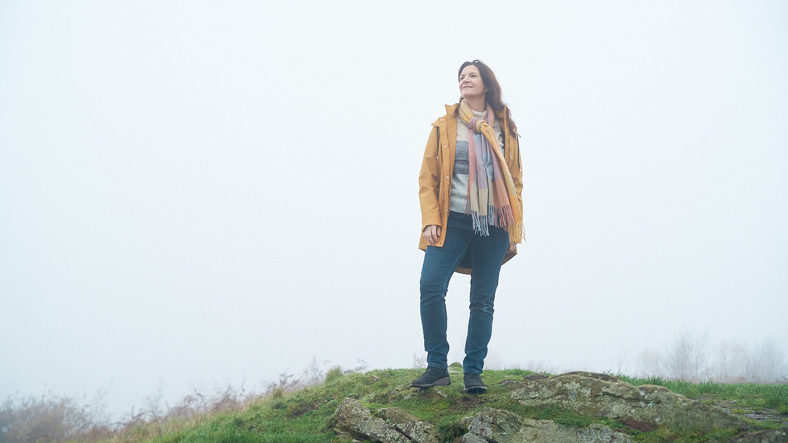 Woman stood on top of a hill looking into distance smiling