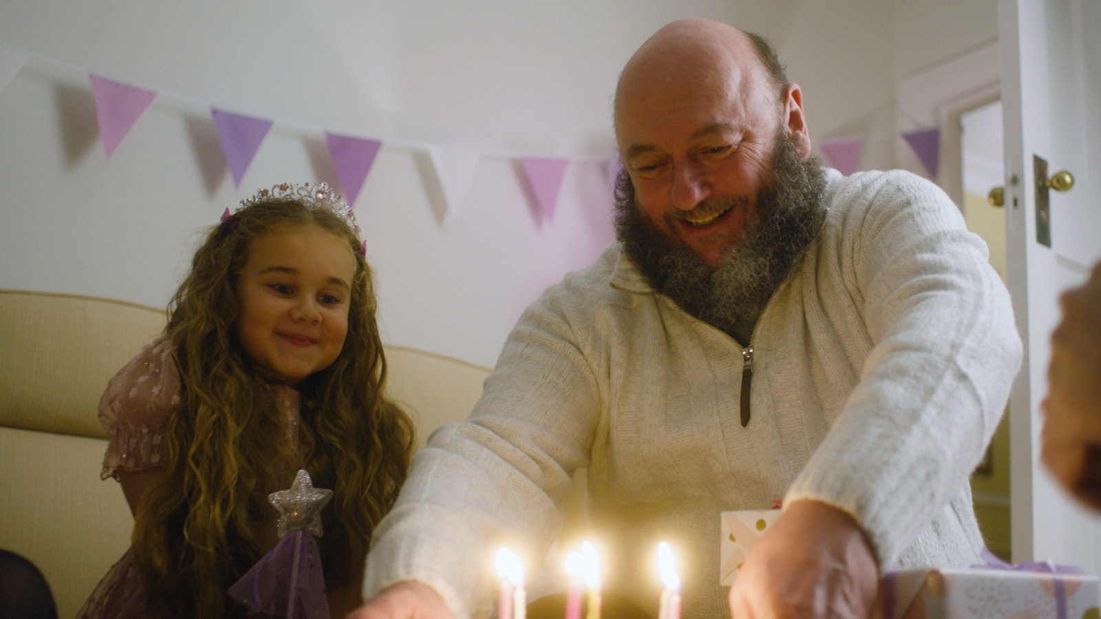 Man placing down birthday cake with candles in front of young girl